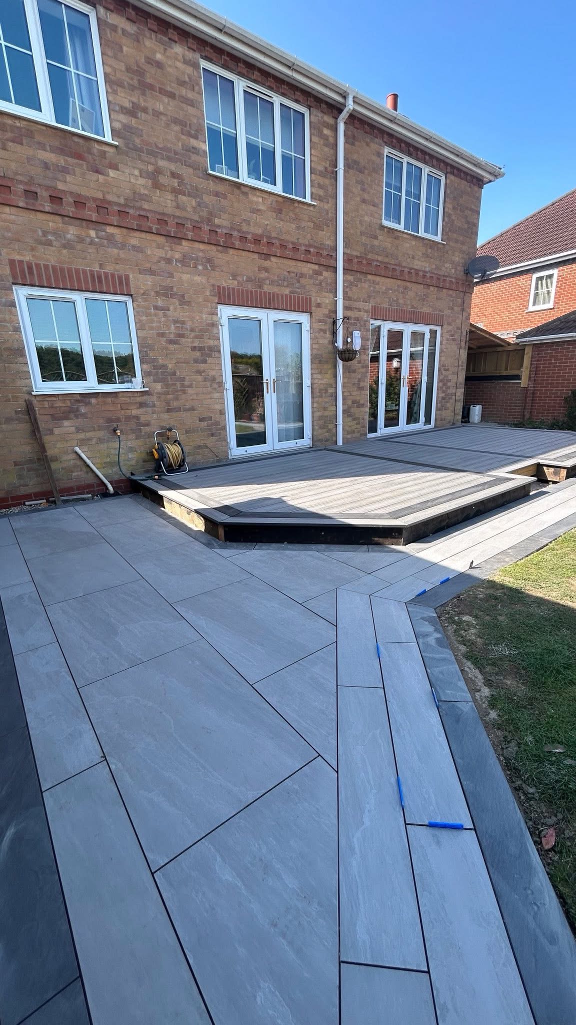 Grey paving around a raised deck beside a brick house