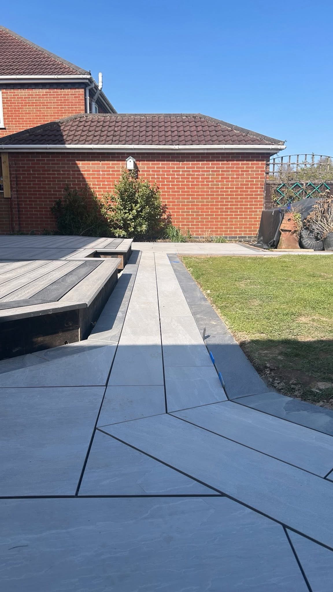 Grey paving and edging alongside a lawn and raised deck